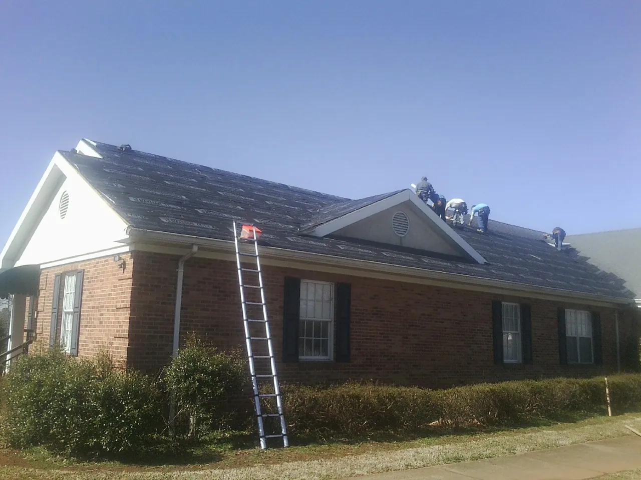 Crew tearing shingles off a brick ranch roof with a ladder set — Emergency Roof Repair work by our crew in Ironside