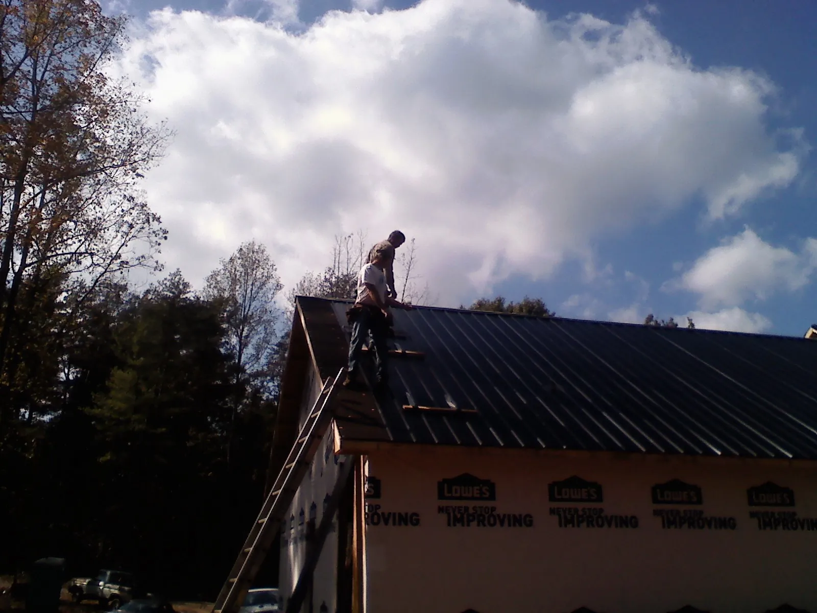 Roofer fastening dark metal panels high against a cloudy sky, from a Roof Inspection job in Ironside